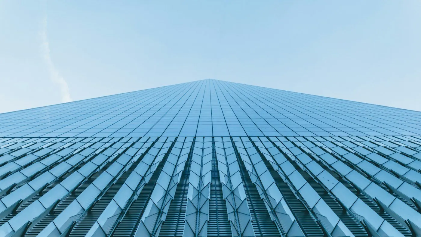 Tall glass skyscraper facade rising into a blue sky